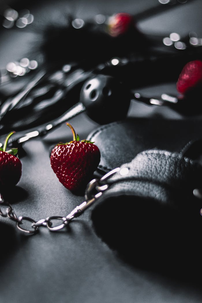Close-up of a strawberry amidst chains and leather on a dark surface, artistic composition.